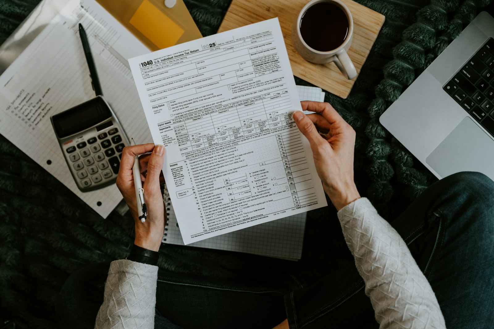 Hands holding claim forms beside a calculator and laptop