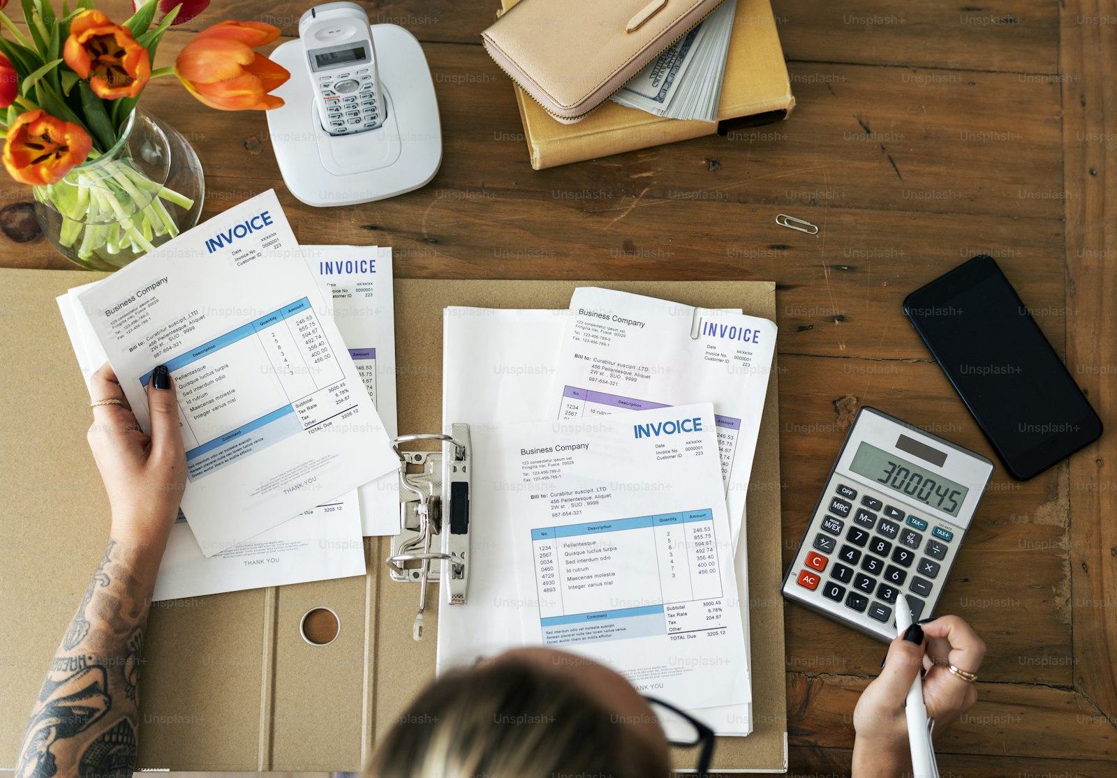 Invoices being reconciled with a calculator and phone on a desk