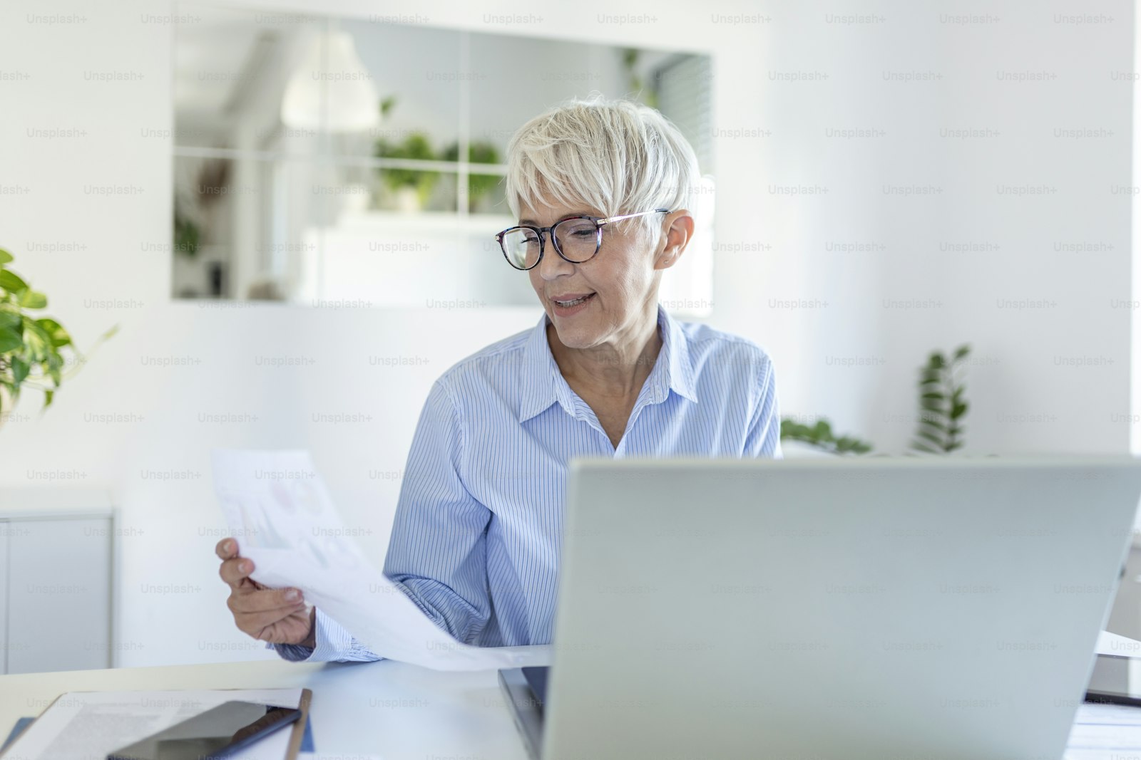 A woman in glasses reviewing a stack of plan documents at her desk