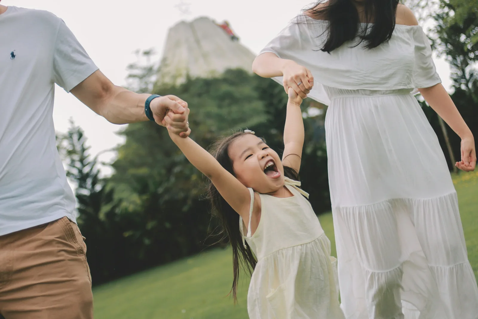A young child laughing while her parents swing her between them outdoors