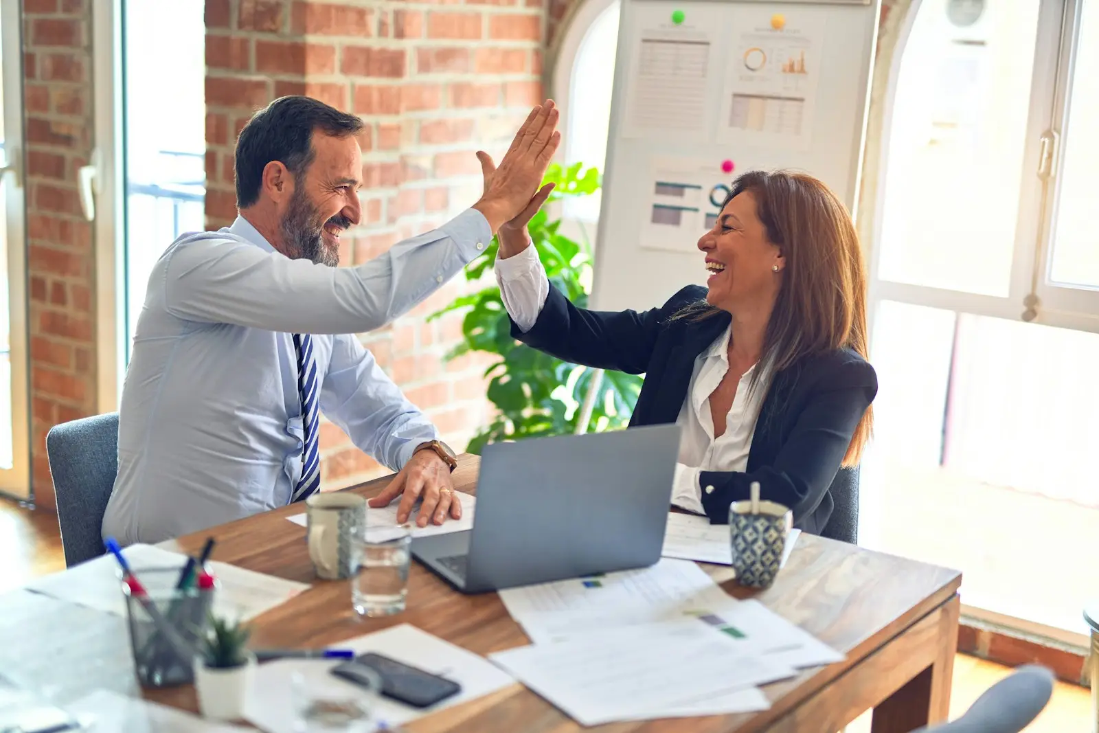 Two colleagues celebrating at a desk; illustrative, not ExpatMedicare staff
